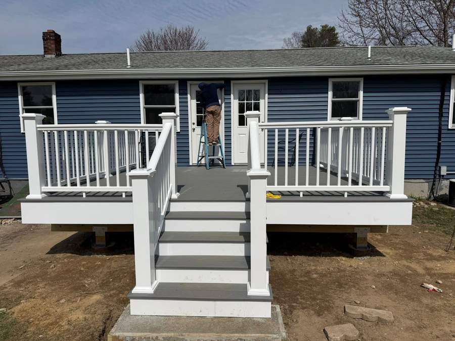 Finished composite deck with white railings and stairs against new blue vinyl siding on a South Shore ranch by CB Builders Corp.
