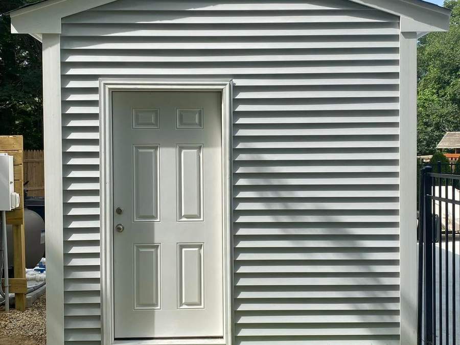 Finished custom shed with light gray vinyl siding, white trim, and a shingle roof by CB Builders Corp. on the South Shore